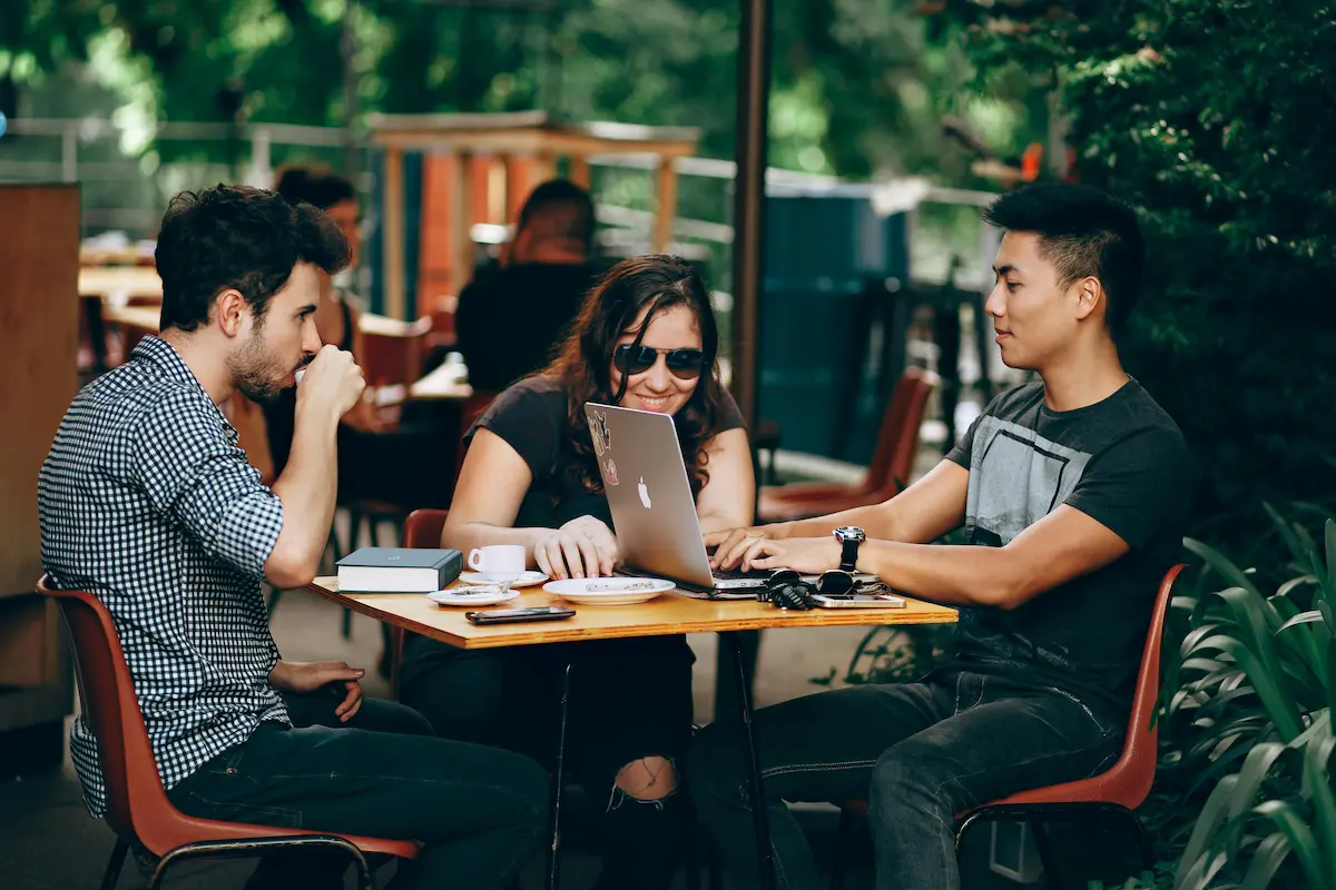 Friends casually gathered outside a café, looking at a laptop together.
